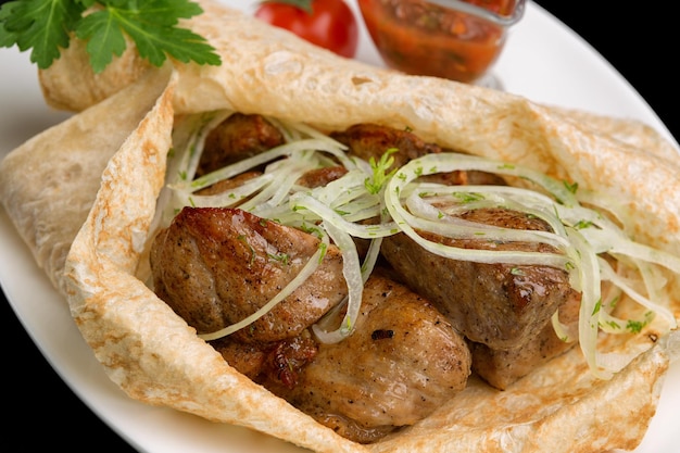 Varkensspiesjes op pitabroodje met saus en uien op een bord