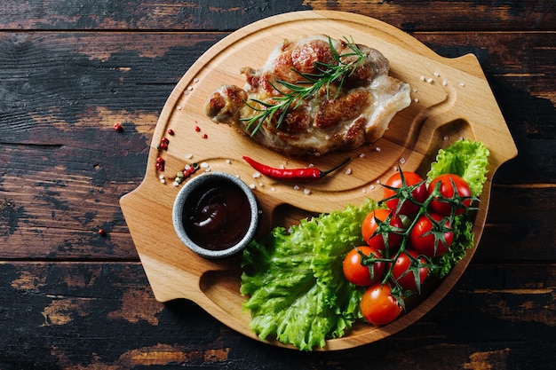 Foto varkenssteak op een houten bord met kerstomaatjes en salade rustieke gerechten