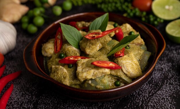 Foto varkensvlees groene curry in een bruine schaal met specerijen op een zwarte cement achtergrond