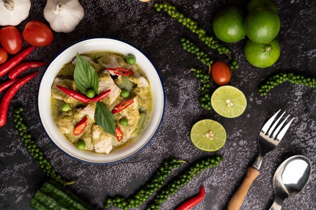 Varkensvlees groene curry in een witte schaal met specerijen op een zwarte cement achtergrond