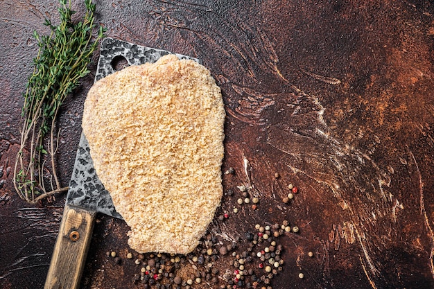 Varkensvlees Rauwe Schnitzel of Schnitzel op een vleesmes met kruiden. Donkere achtergrond. Bovenaanzicht. Ruimte kopiëren.