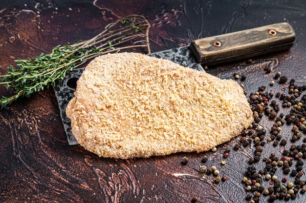 Varkensvlees Rauwe Schnitzel of Schnitzel op een vleesmes met kruiden. Donkere achtergrond. Bovenaanzicht.