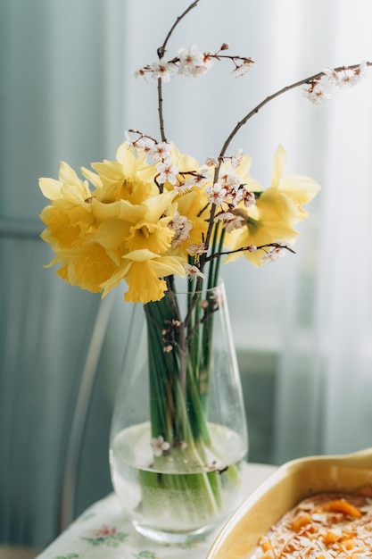 A vase of daffodils sits on a table with a yellow cloth.