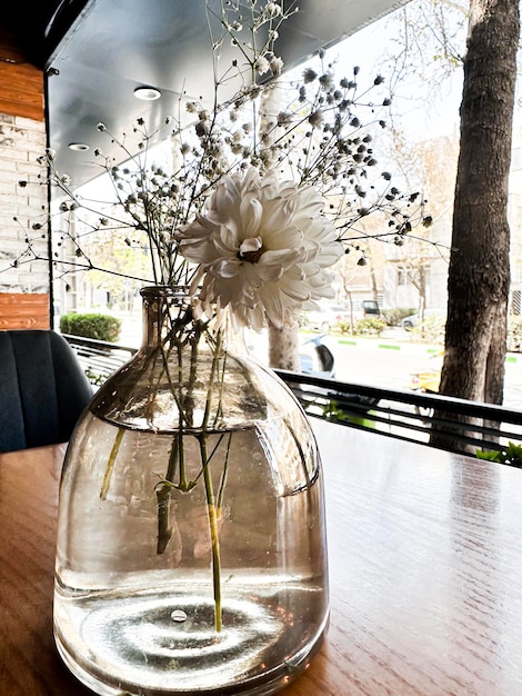 A vase of flowers sits on a table with a street in the background.