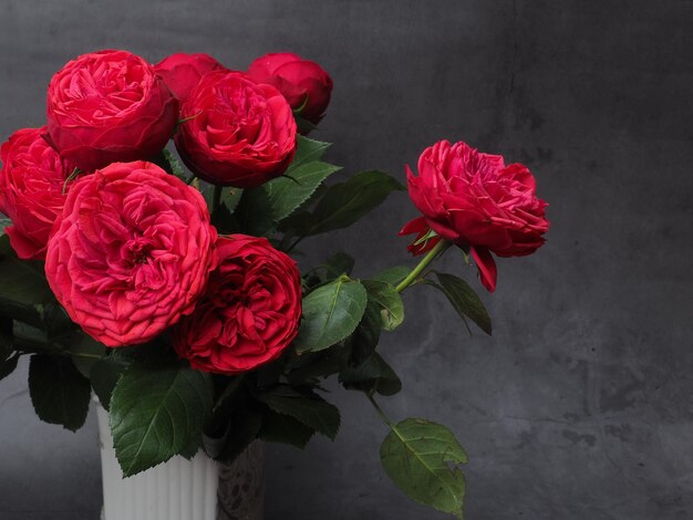 A vase of red roses with a green leaf on the stem.