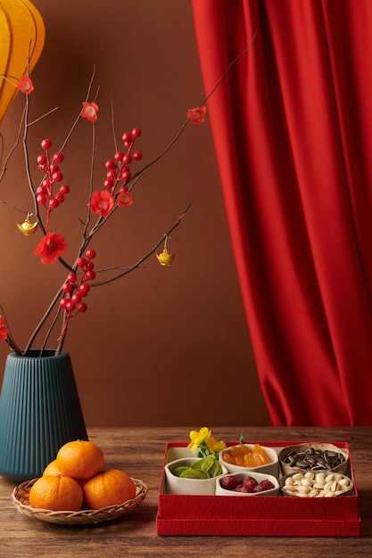 Vase with blooming branches next to box of nuts and candied fruits prepared for chinese new year cel...