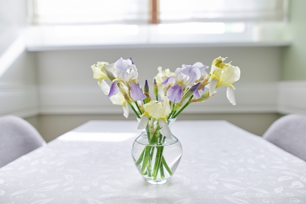 窓の近くのテーブルに黄色と紫の菖蒲の花束と花瓶