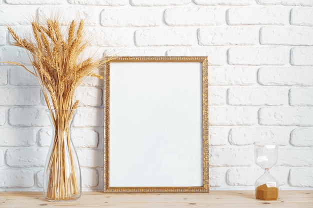 Vase with ears of wheat and photo frames against brick wall