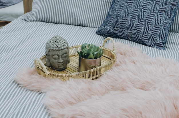 Vase with a flower and buddha head on rustic wooden serving tray with blanket. 