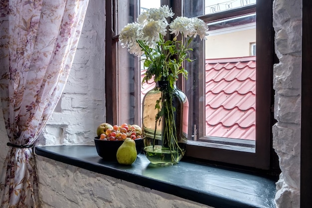Фото Ваза с цветами на подоконнике в старом винтажном стиле с фруктами или свечами