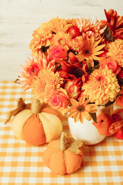 Vase with flowers and small orange textile pumpkins on a table