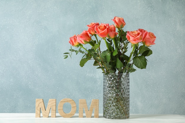 Vase with orange roses and inscription Mom on white table