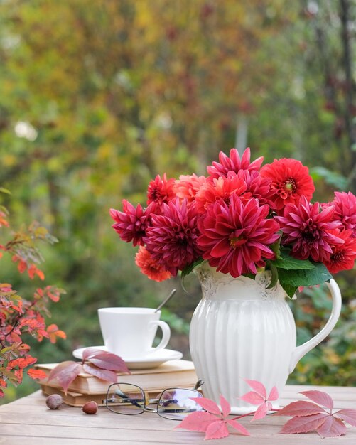 Vase with red autumn flowers and books on the table in the autumn garden Autumn still life