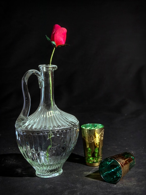 A vase with a rose on it and a glass on the table