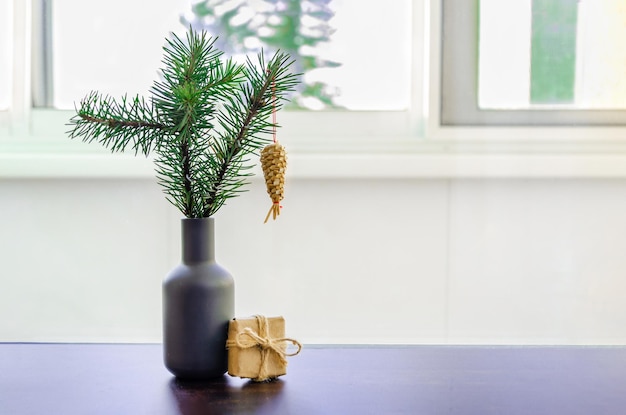 가문비나무 나뭇가지가 있는 꽃병 크리스마스 빨대 장난감 선물이 창문 배경에 있는 친환경 포장에 담겨 있습니다.
