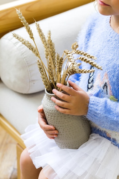 Vase with wheat in children's hands The concept of beautiful and stylish home decor