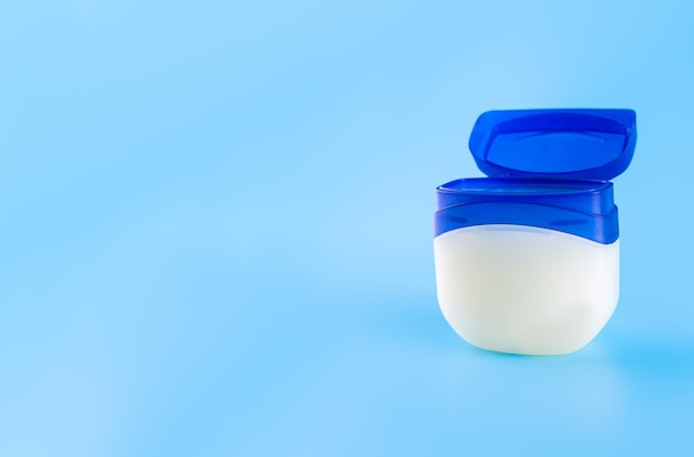 Vaseline or petroleum jelly in a clear jar on blue background with copy space Skin care ointment