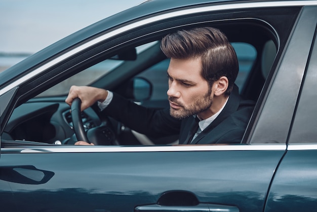 Vast in het verkeer. knappe jonge man in volledig pak die er recht uitziet tijdens het autorijden