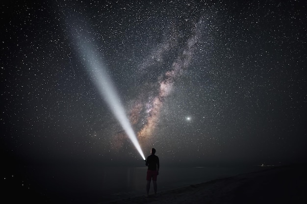 Foto sotto l'immenso cielo stellato giace un esploratore che con un raggio di luce svela i misteri del mondo cosmico da una riva silenziosa