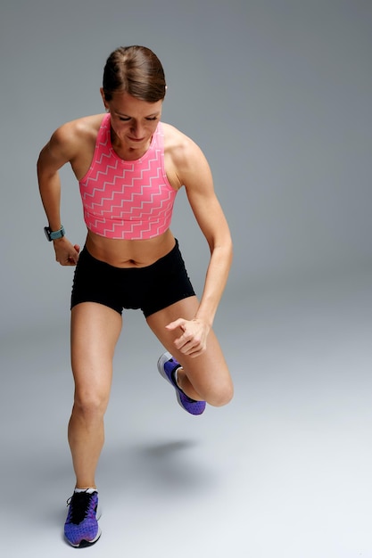 Vastberaden gespierde vrouwelijke atleet training been verhogen en rekoefeningen doen Sport vrouw in sportkleding opleiding binnenshuis doen fitness aerobics grijze achtergrond