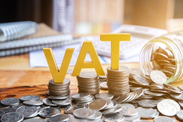 Vat Concept. Word vat with stacked coins there is a notebook calculator on the desk.