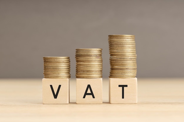 VAT word in wooden blocks with coins stacked in increasing stacks Vat increasing concept Copy space