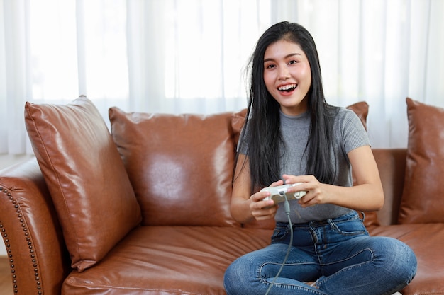 VDO game console station concept. active asian woman sitting on sofa, holding joystick and playing exciting game. Cute girl looked excited with game controller console