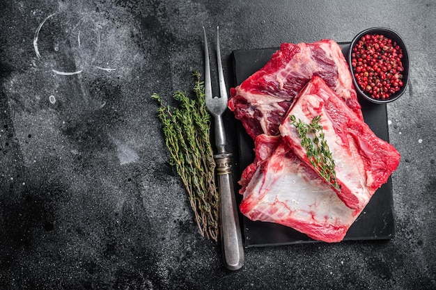 Veal beef Short Ribs, raw sparerib on marble board. Black background. Top view. Copy space.