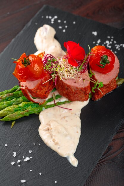 Veal medallions with asparagus on black dishware on wooden table