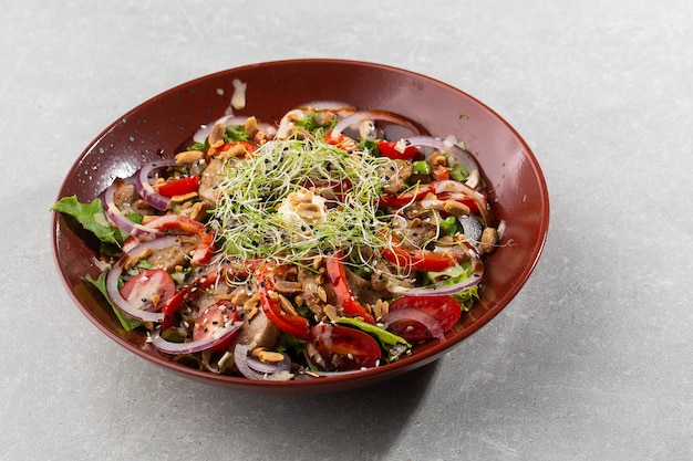 Veal salad with cherry tomatoes, mushrooms on a black plate on dark