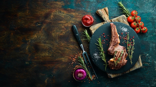 Veal steak on the bone with spices thyme and rosemary top view\
flat lay top view on black stone cutting table