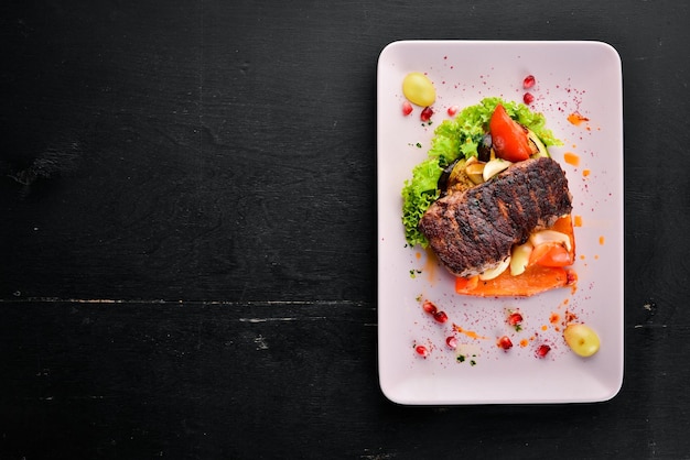 Veal steak on a plate of vegetables On a wooden background Top view Free space for your text