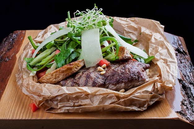 Veal steak with rocket and Parmesan cheese in parchment on wooden board