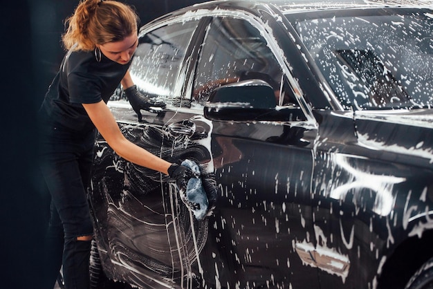 Veegt voertuig af dat in witte zeep zit Moderne zwarte auto wordt schoongemaakt door een vrouw in het wasstation