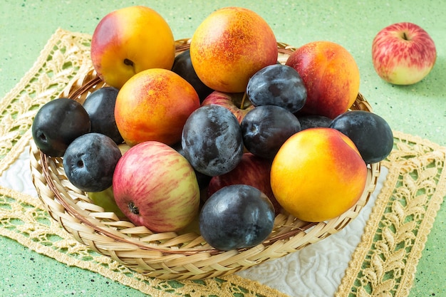 Veel biologische rijpe pruimen nectarines en appels in rieten mand op groene achtergrond