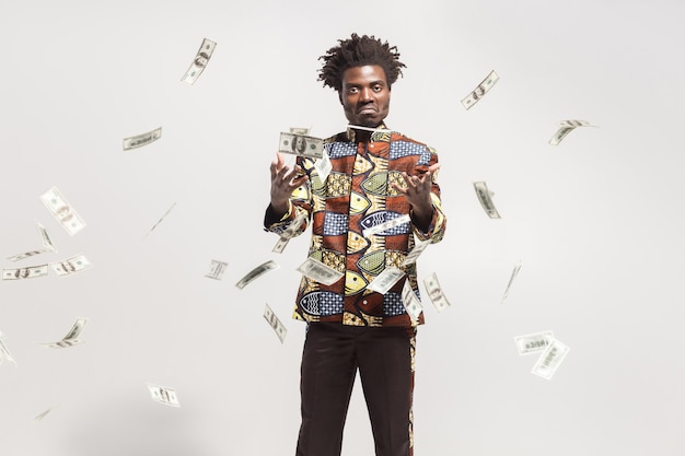 Veel contant geld vliegt in de buurt van Afrikaanse man in nationaal kongo-kostuum. Binnen, geïsoleerd op grijze achtergrond