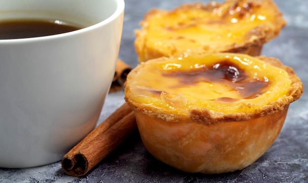 Veel desserts, pastel de nata of Portugese eiertart en kaneelstokjes met een kop koffie.