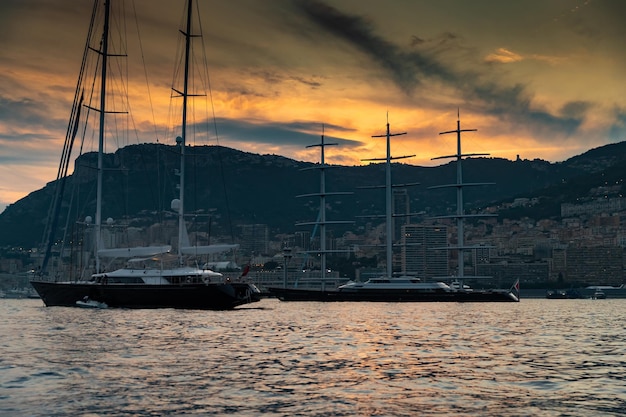 Veel enorme zeiljachten en motorboten in de haven van Monaco bij zonsondergangbergen zijn op de achtergrond me...