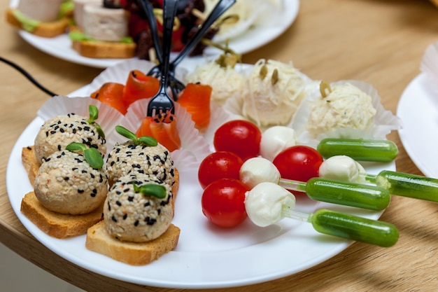 Veel hapjes met kaas en groenten op de witte plaat op de houten tafel.
