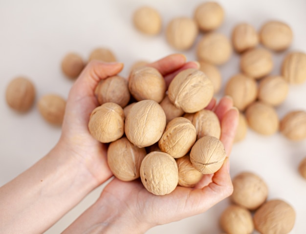 Veel hele walnoten in handen van vrouwen op een witte achtergrond close-up. Gezonde, biologische voeding met een hoog gehalte aan eiwitten en eiwitten.