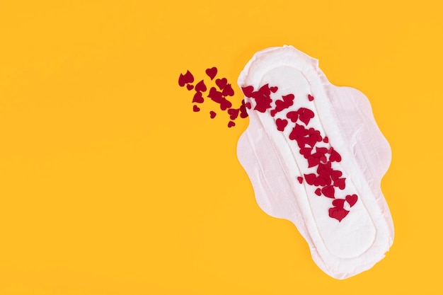 Veel kleine rode harten, symbolen van de menstruatiecyclus, op een vrouwelijk maandverband. Producten voor vrouwelijke hygiëne tijdens de menstruatiecyclus. Gele achtergrond. Ruimte kopiëren. Hoge kwaliteit foto