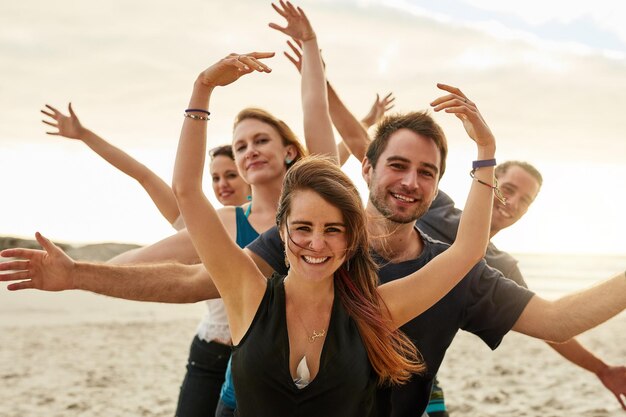 Veel lichamen één hart Portret van een groep gelukkige jonge vrienden die samen poseren met hun armen omhoog op het strand