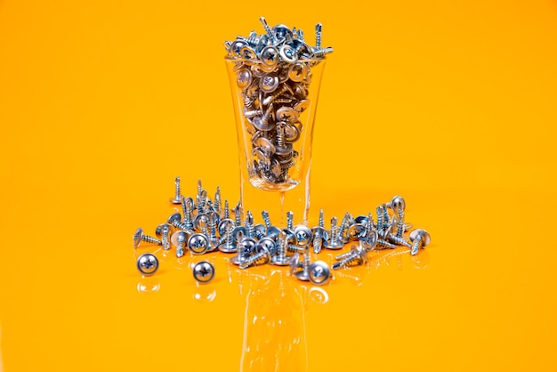 Veel metalen zelftappende schroeven gemaakt van staal in een glas in emmer pot zelftappende schroef voor metaal voor ijzer verchroomde zelftappende schroef op een oranjegele achtergrond