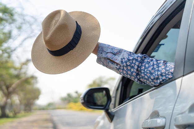 Veel plezier en vrijheid tijdens een reis met opgeheven hand en met een mooie hoed buiten de raamauto in de zomervakantie