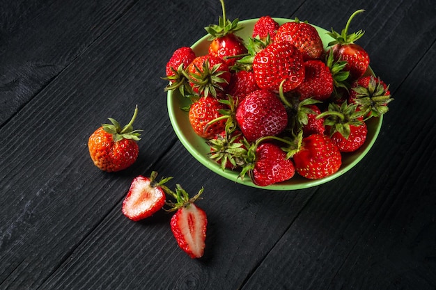 Veel rode rijpe aardbeien in een bord op zwarte vintage tafel. Zomerdieet en vitamine set idee.