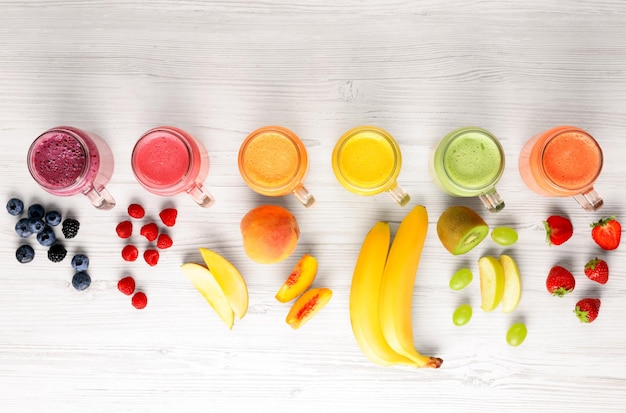 Veel verschillende smakelijke smoothies en ingrediënten op witte houten tafel plat gelegd