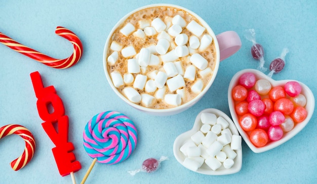 Veel verschillende snoepjes op een blauwe achtergrond en een kop warme chocolademelk met marshmallows