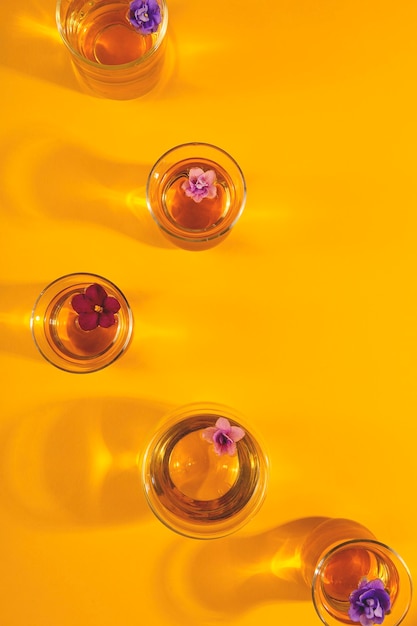 Veel verschillende transparante kopjes thee met bloemen op een gele achtergrond. kopieer ruimte
