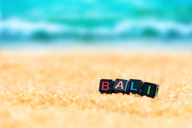 Foto veelkleurig woord bali van zwarte blokjes in het zand op de achtergrond van strand en zee