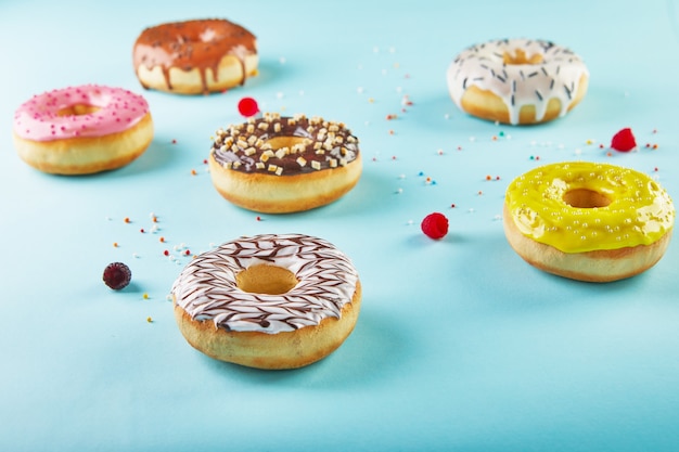 Veelkleurige donuts met glazuur en hagelslag op blauwe achtergrond.